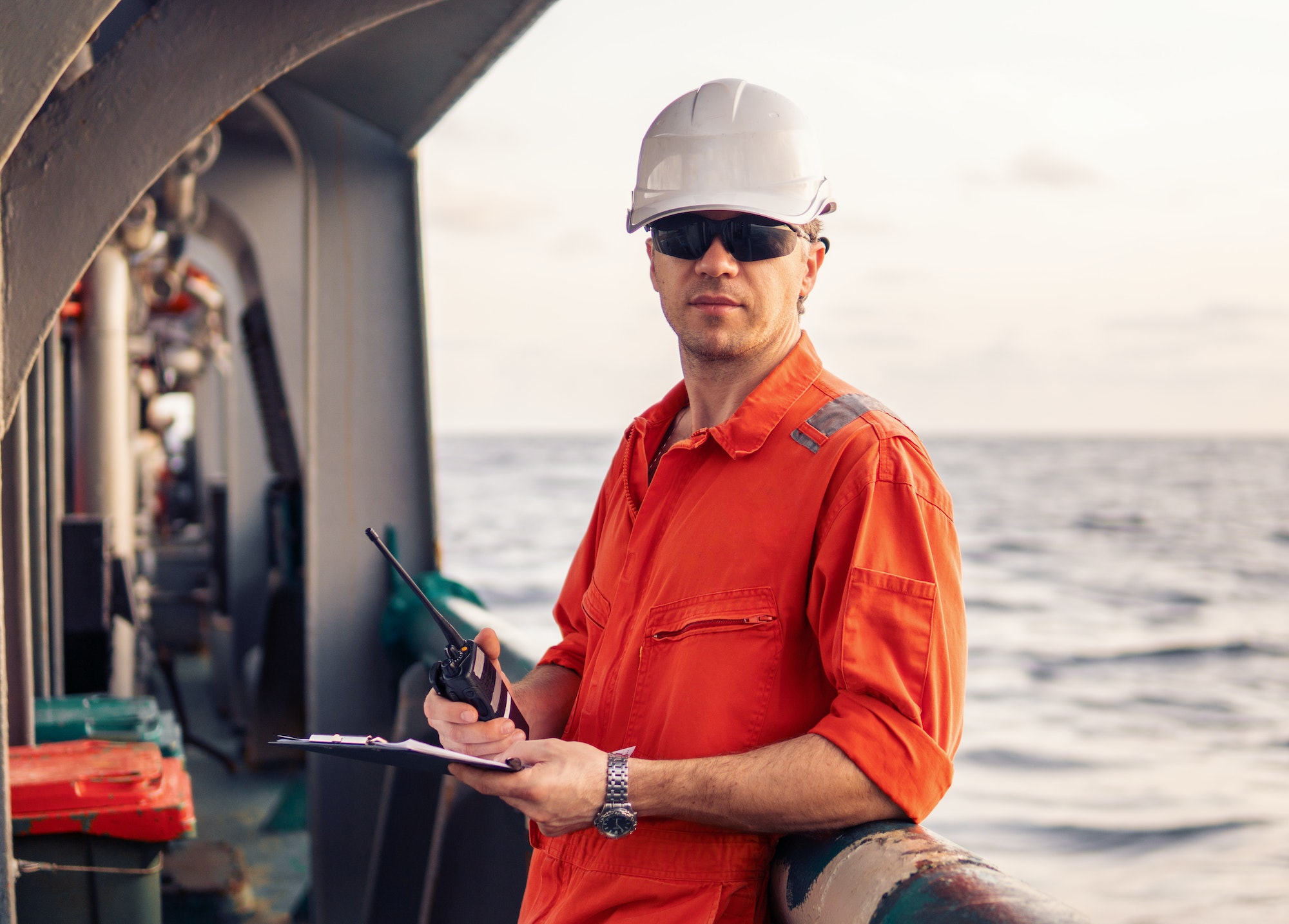 Deck Officer on deck of offshore vessel holds VHF walkie-talkie radio