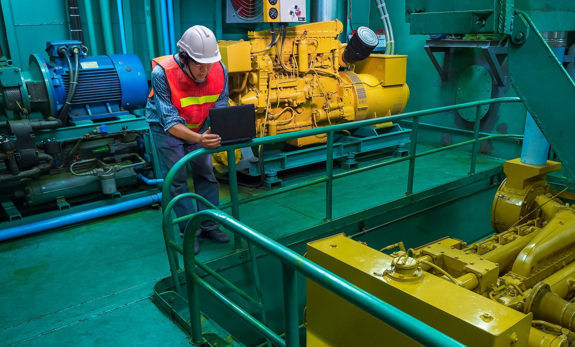 Engineer using laptop computer to checking engine quality inside of engine room of fishing vessel